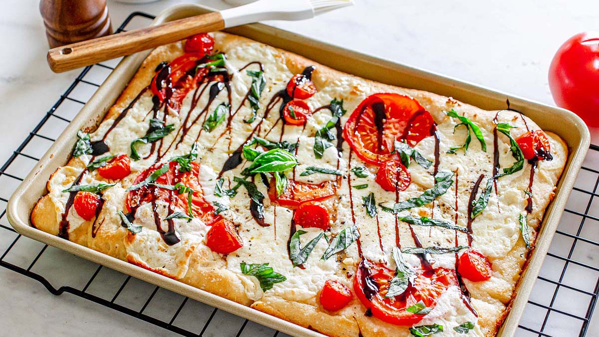 A sheet pan pizza topped with mozzarella, tomatoes, and basil.