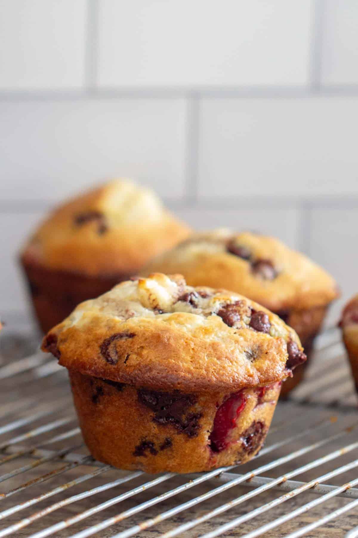 Close-up of chocolate chip muffins cooling on a wire rack, set against a tiled background.